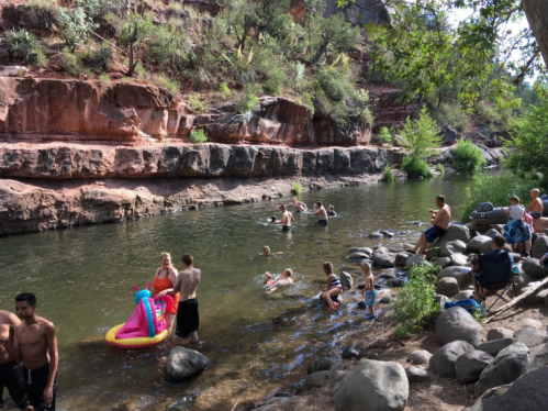 People enjoying a sunny day by a river, swimming, relaxing on rocks, and using an inflatable float.