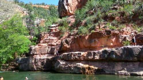 A scenic river surrounded by rocky cliffs and lush greenery, with people swimming and climbing nearby.