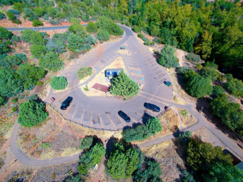Aerial view of a parking lot surrounded by trees and shrubs, with several parked vehicles and winding pathways.