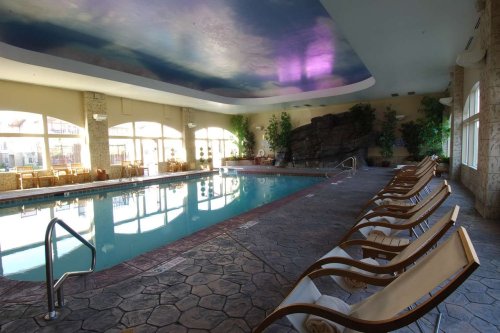 Indoor swimming pool with a stone deck, lounge chairs, and large windows letting in natural light.