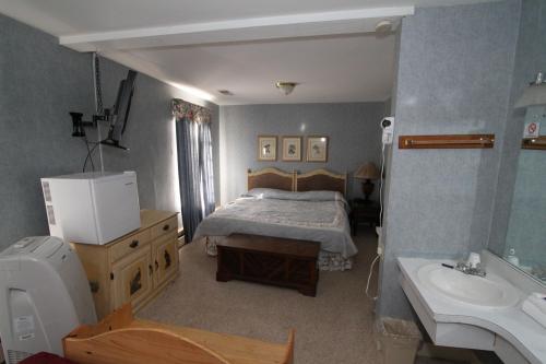 A cozy hotel room featuring a bed, dresser, TV, and a small bathroom area with a sink.