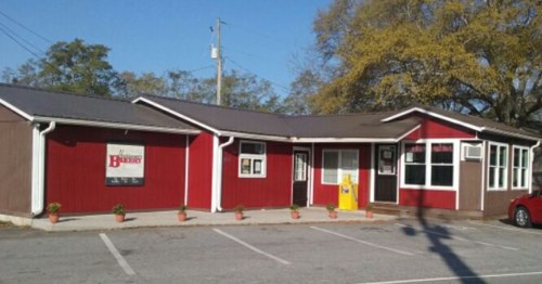 A red and brown building with a sign, surrounded by small potted plants and parked cars.