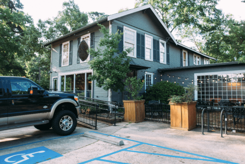 A gray two-story building with large windows, surrounded by trees, and a black truck parked in a designated area.