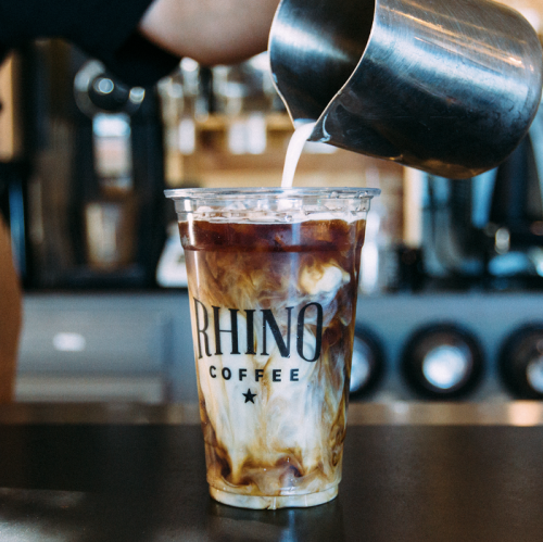 A barista pours milk into a cup of iced coffee from Rhino Coffee, creating a swirled effect.