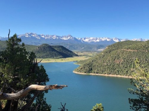 A serene landscape featuring a river winding through green hills, with snow-capped mountains in the background under a clear blue sky.