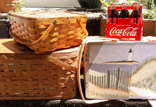 A woven picnic basket, a wooden box, and a Coca-Cola six-pack beside a beach-themed illustration on a tray.