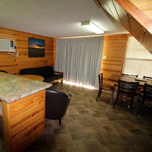 Cozy wooden interior of a cabin with a seating area, dining table, and large window with curtains.