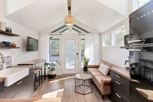 Cozy interior of a modern tiny home with a sofa, plants, and large windows letting in natural light.