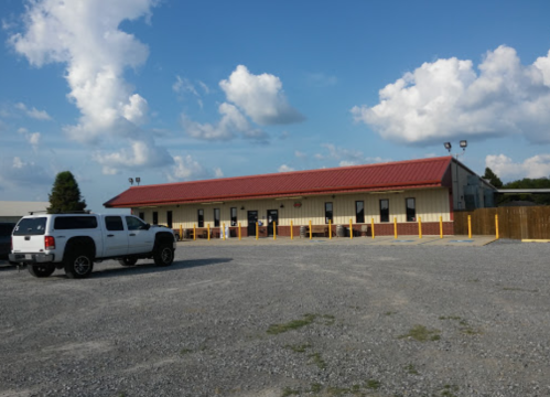 A single-story building with a red roof, surrounded by gravel and a white truck parked in front under a blue sky.