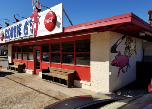 A colorful restaurant exterior with red accents, featuring a pig mural and Coca-Cola signage. Benches are outside.