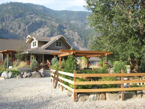 A charming house with a wooden fence and garden, set against a backdrop of mountains and greenery.