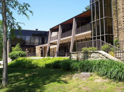 Modern building with large glass windows, stone accents, and landscaped greenery in front on a sunny day.