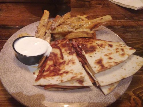 A plate with quesadillas, a side of fries, and a small cup of dipping sauce.