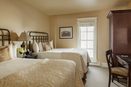 Cozy hotel room with two beds, a desk, and a window, featuring warm tones and elegant decor.