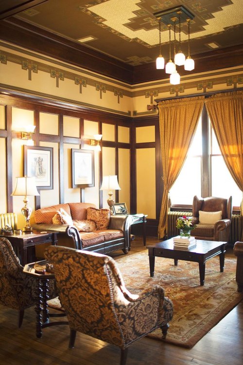 Cozy living room with elegant decor, featuring a patterned rug, armchairs, a sofa, and warm lighting.