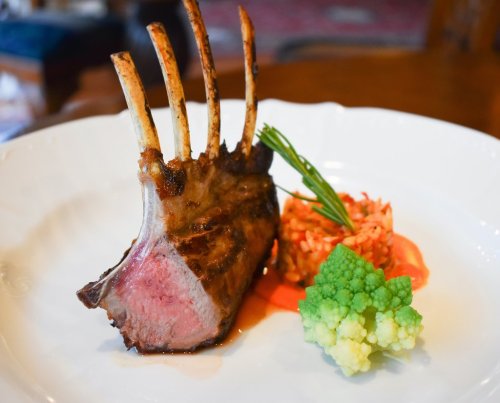 A beautifully plated rack of lamb with a side of colorful vegetables and a garnish of herbs.