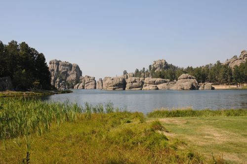 A serene lake surrounded by large rock formations and lush greenery under a clear blue sky.
