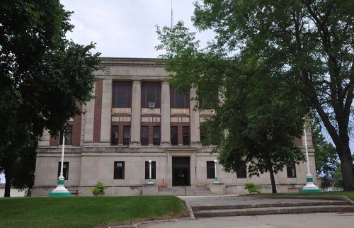 Historic building with a stone facade, large windows, and trees in front, set against a cloudy sky.