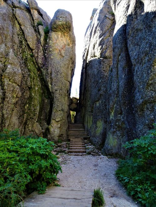 A narrow passage between towering rock formations, with wooden steps leading through lush greenery.