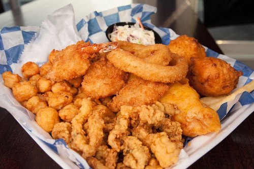 A basket of fried seafood including shrimp, fish, onion rings, and hushpuppies, served with coleslaw.