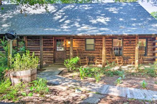 A rustic log cabin with a porch, surrounded by greenery and a wooden walkway leading to the entrance.