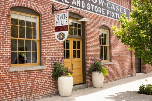 Exterior of Seven Hills Winery, featuring a brick building, yellow door, and potted plants by the entrance.