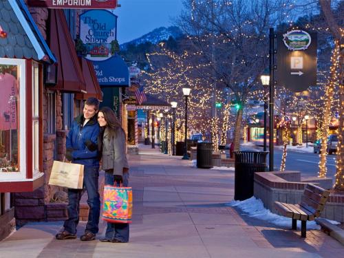 A couple strolls down a festive street, holding shopping bags, surrounded by twinkling lights and winter scenery.