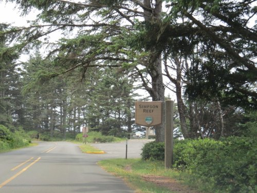 Sign for Simpson Reef along a tree-lined road, with a parking area visible in the background.