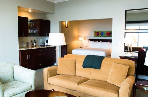 A cozy hotel room featuring a sofa, kitchenette, and a bed in a separate area, with warm lighting and modern decor.