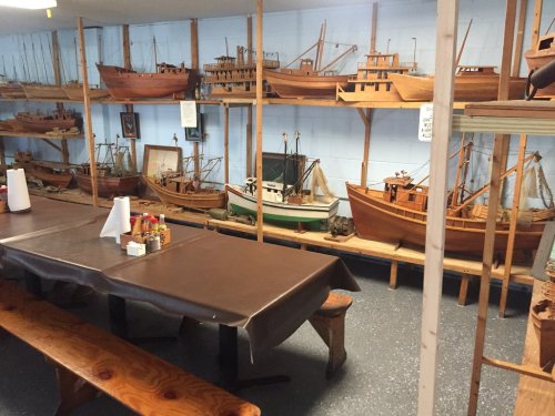A room with wooden model ships displayed on shelves, alongside a table set with condiments.