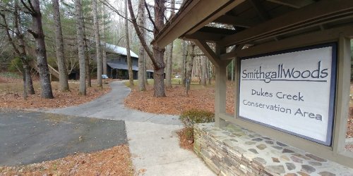 Sign for Smithgall Woods at Dukes Creek Conservation Area, surrounded by trees and a winding path.