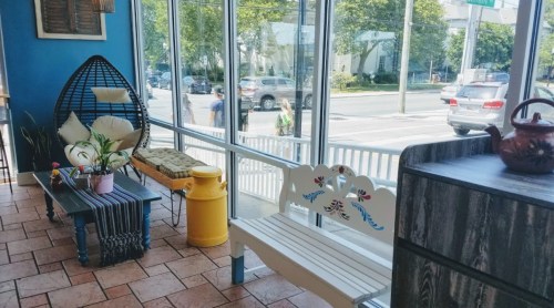 Bright interior with large windows, colorful seating, and a decorative teapot on a counter.