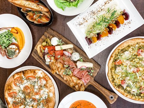 A spread of various dishes including pizza, charcuterie, salads, and colorful appetizers on a wooden table.