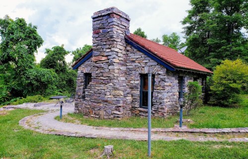 A small stone cottage with a chimney, surrounded by greenery and a winding path.