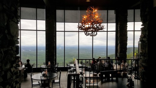 A restaurant interior with stone walls and large windows showcasing a scenic mountain view.
