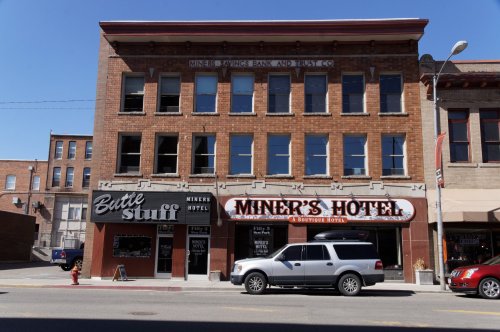 Historic brick building featuring Miner's Hotel and Miner's Savings Bank, with a parked SUV in front.