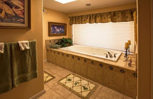A spacious bathroom featuring a large bathtub, decorative tiles, and soft lighting with plants and artwork.