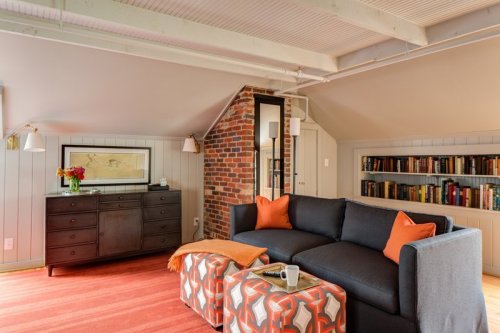 Cozy living room with a gray sofa, orange accents, a brick chimney, and a bookshelf against the wall.