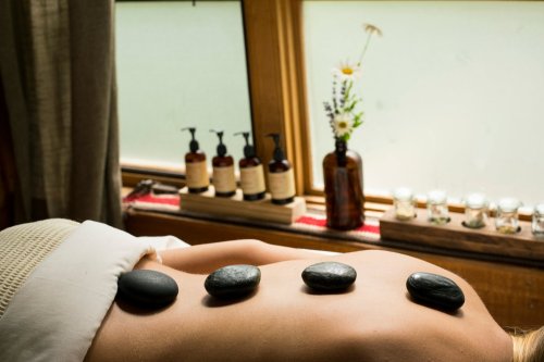 A person receiving a hot stone massage with smooth stones placed on their back, surrounded by a serene spa setting.