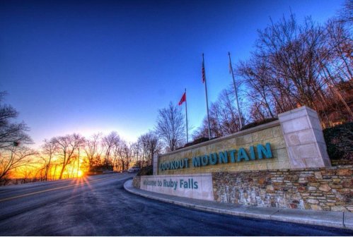 Sign for Lookout Mountain at sunset, with trees and flags in the background, welcoming visitors to Ruby Falls.
