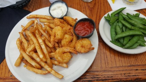 A plate of golden fried shrimp and French fries with dipping sauces, alongside a side of fresh green snap peas.