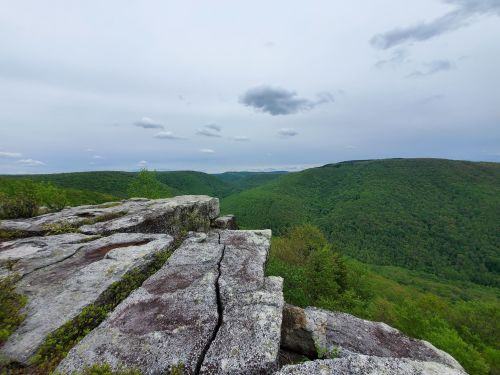 A rocky outcrop overlooks lush green hills under a cloudy sky, showcasing a serene natural landscape.