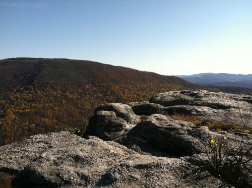 A rocky outcrop overlooks a colorful autumn landscape with rolling hills and clear blue skies.