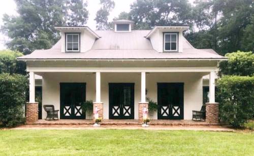 A charming two-story house with a porch, surrounded by greenery and featuring black doors and white walls.
