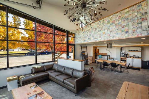Modern interior of a cozy space with large windows, a leather sofa, and colorful wall art, surrounded by autumn trees.