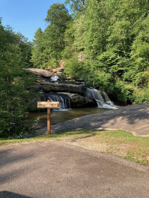 A serene view of a waterfall at Hansey Creek, surrounded by lush green trees and rocky terrain.