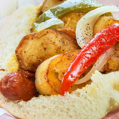 A close-up of a sandwich filled with grilled vegetables, including peppers and onions, alongside fried potatoes.