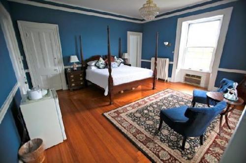 Cozy bedroom with blue walls, a four-poster bed, two chairs, a small table, and a window letting in natural light.