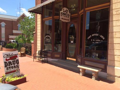 Exterior of a historic drugstore museum with a sign, benches, and a brick walkway on a sunny day.