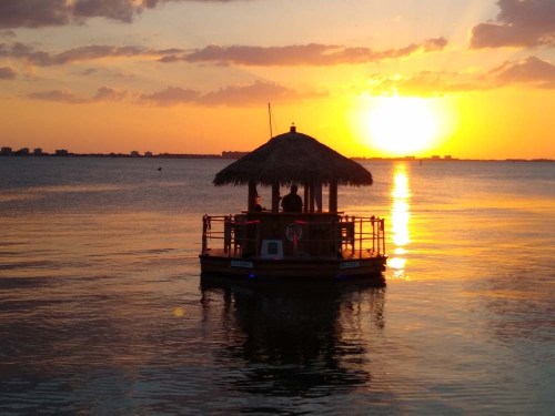 A small hut on a floating platform at sunset, reflecting golden light on calm water.